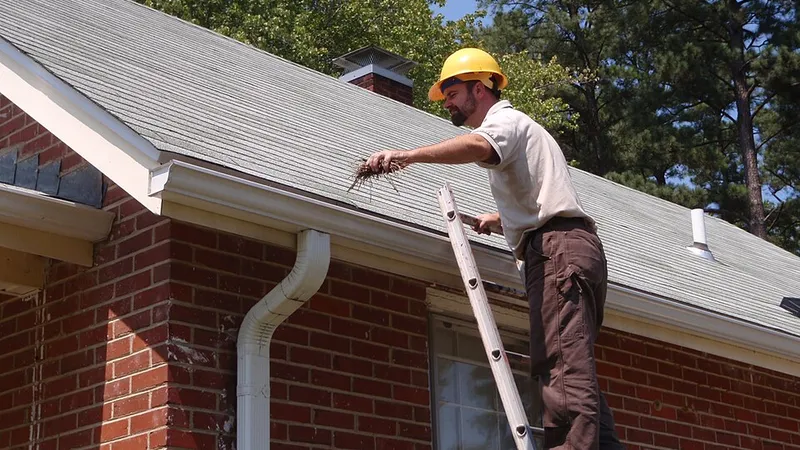 Worker on a ladder cleaning a house gutter