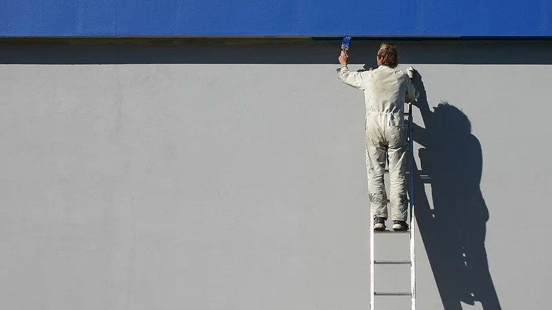 Painter on a ladder painting an exterior wall